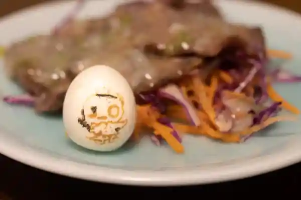紫キャベツと人参サラダの上にネギ塩牛タンを盛り付けた写真です。手前にはうずらのゆで卵がそえられています。容器は薄い水色の丸皿です。