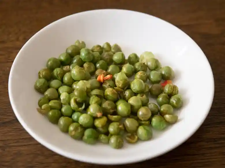 白い皿に麻辣青豆がもられています。緑色のグリーンピースに混じって、赤色の花椒が見えます。