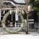 神社の本殿前に建てられた茅の輪の写真です。茅を束ねた直径が6尺4寸（約194cm）の茅の輪が建っています。茅の輪の両脇には神社名が描かれた提灯と狛犬が並んでいます。