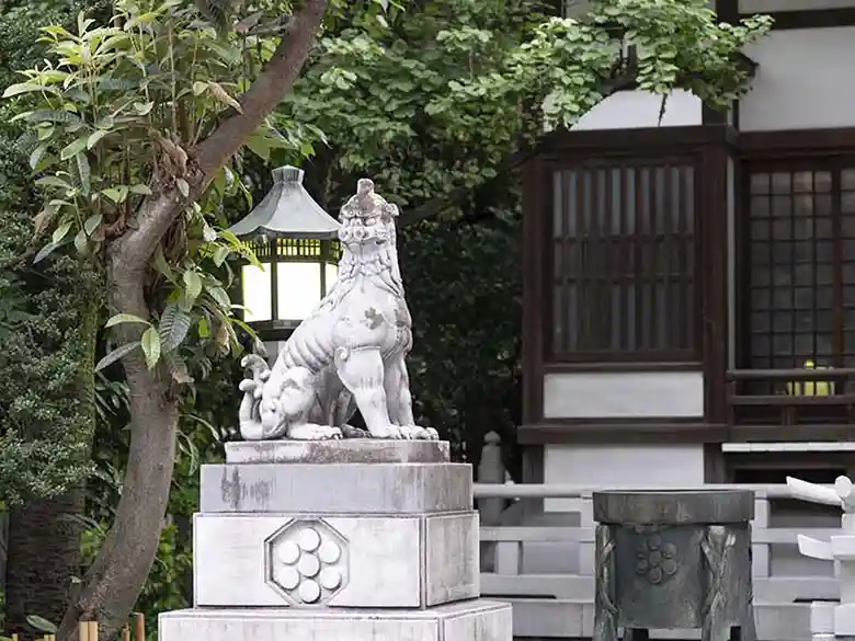 神社の本殿前に設置された狛犬の写真です。2mほどの高さの石台の上に白色の石で作られた1m高の狛犬が鎮座しています。狛犬は天に向かって吠えています。