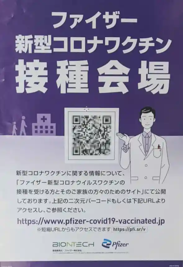 新型コロナワクチンの接種会場に置かれ看板の写真です。紫色の地に、白い文字で「ファイザー 新型コロナワクチン接種会場」と書かれています。白衣を着た男性医師のイラストが描かれています。