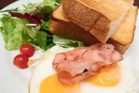 This photo shows the Fried Eggs set. It consists of two bacon and eggs, salad, and two slices of toast on a white plate. The toast is a bread called Bulman. It is a soft and moist bread.