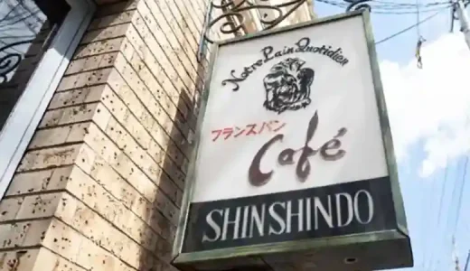 The photo shows a sign posted at the storefront of the cafe "Shinshindo" in front of Kyoto University's North Gate. The words "Notre Pain Quotidien" and "café" are written in French, and "French bread" is written in Japanese. Notre Pain Quotidien" means "our daily bread" in French.