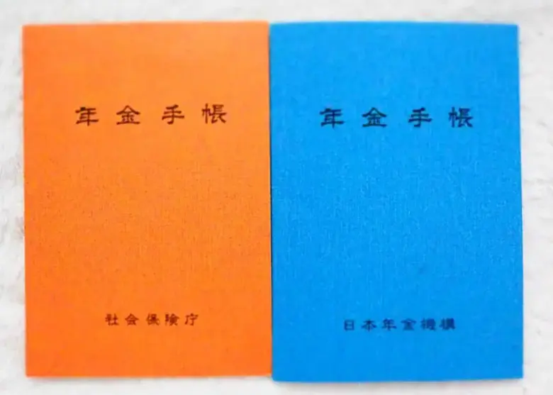 国民年金手帳の写真です。表紙の色がオレンジとブルーの手帳が並んでいます。オレンジ色の手帳は1974年11月から1997年1月まで発行されました。その後は現在までブルーの手帳が使われています。