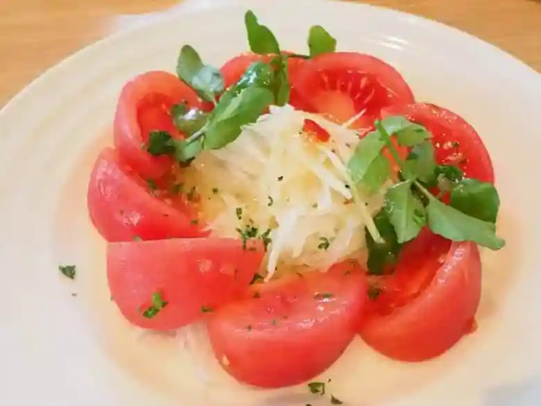 トマトサラダの画像です。白くマルイお皿に6等分に切ったトマトと千切りの玉葱、クレソンが盛られています。白、赤、緑の色合いが鮮やかです。