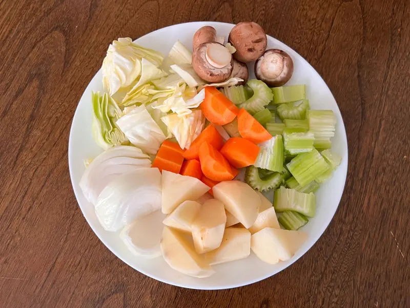切り刻んだ野菜の写真です。白い皿の上に刻まれたマッシュルームとセロリ、キャベツ、にんじん、じゃがいも、玉ねぎが並んでいます。