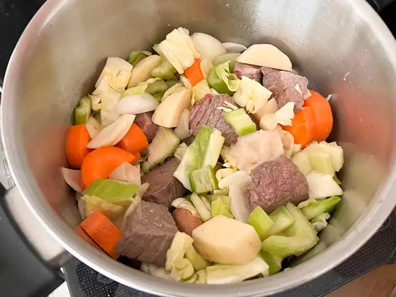 牛肉を炒めている鍋に切り刻んだ野菜を加えた写真です。牛肉の色は薄い茶色に変わっています。﻿