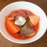 白い皿によそったボルシチにサワークリームを添えた写真です。赤いスープの中にビーツとキャベツ、じゃがいも、にんじんが見えます。