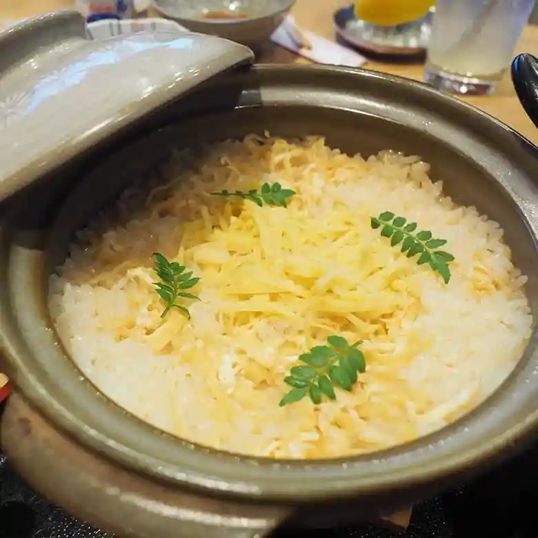 土鍋に入った筍ご飯の写真です。筍ご飯の表面には錦糸卵と木の芽が添えられています。