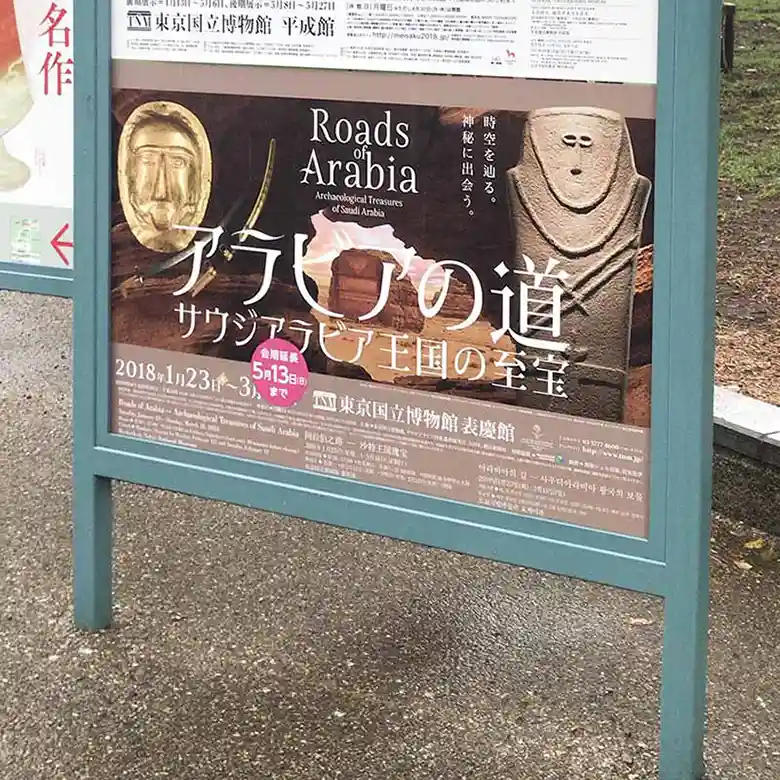 上野恩師公園に掲げられた東京国立博物館のポスターの写真です。表慶館で「アラビアの道－サウジアラビア王国の至宝」が開催中であると告知されています。ポスターには「アラビアの人形石柱」と「葬送用マスク」の写真が写っています。