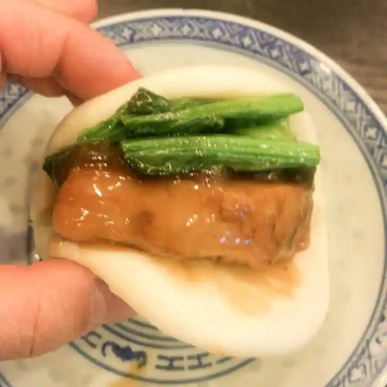 This photo shows eating a Chinese sandwich. Dongpo pork and greens are rolled into the Chinese bread.