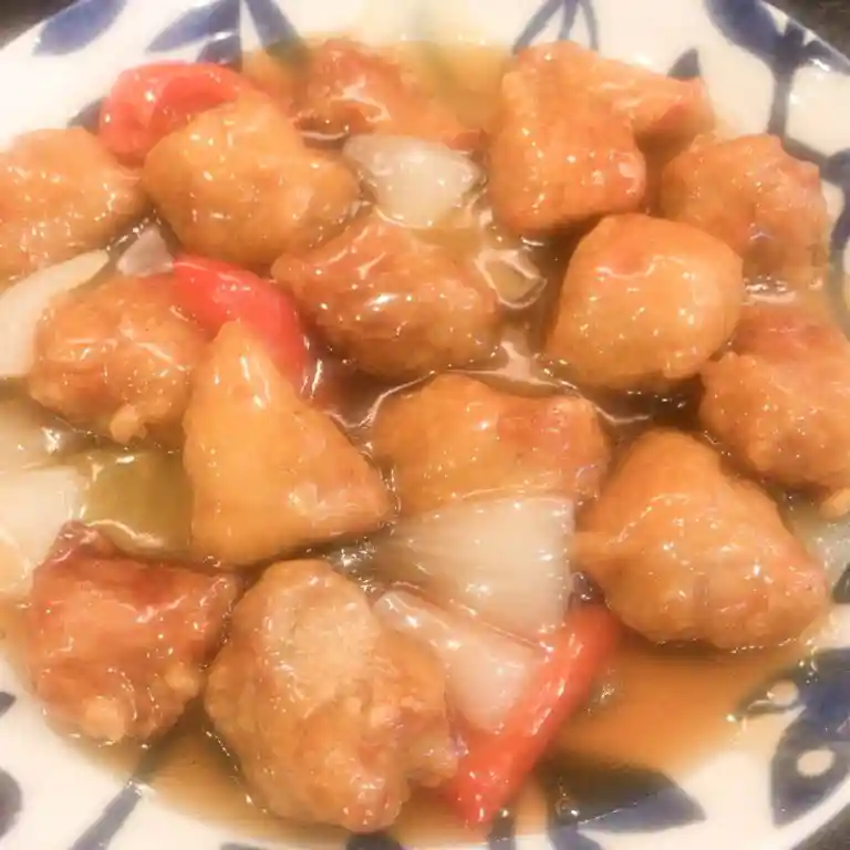 This picture shows a plate of sweet-and-sour pork. It contains a lot of large pieces of meat. Other ingredients besides the meat are pineapple, onions, and carrots.