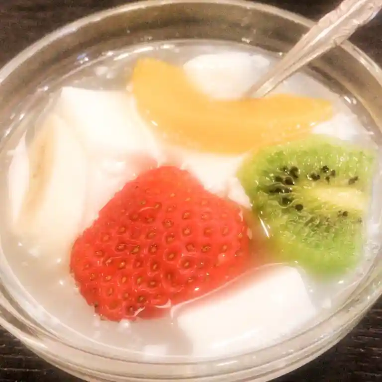 This picture shows Almond Jerry in a glass bowl. Inside the bowl are white-colored hardened apricot powder, strawberries, kiwi, and peaches.
