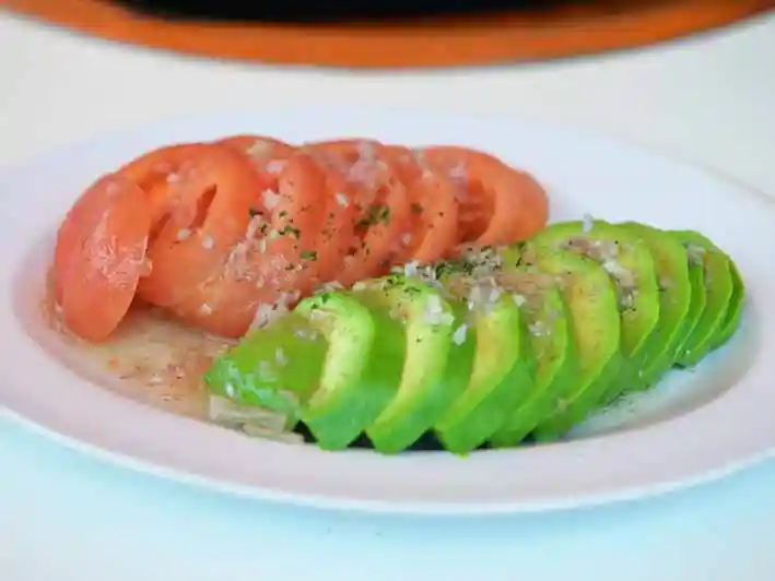 アボカドとトマトのサラダの写真です。白い皿に赤いトマトと緑のアボカドが盛られています。色が鮮でとても綺麗なサラダです。