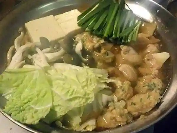 すべての具材が入った鶏ちゃんこ鍋の写真です。銀色の鍋の中に鶏団子、角切りした鶏もも肉、白菜、もめん豆腐、しめじ、ニラが入っています。