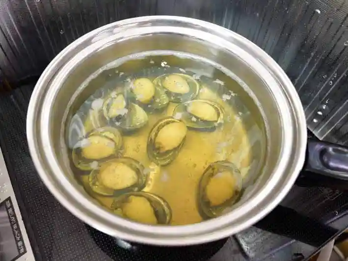 トコブシを煮ている写真です。汁の中にトコブシは沈んでいます。汁は透明で薄い茶色をしています。