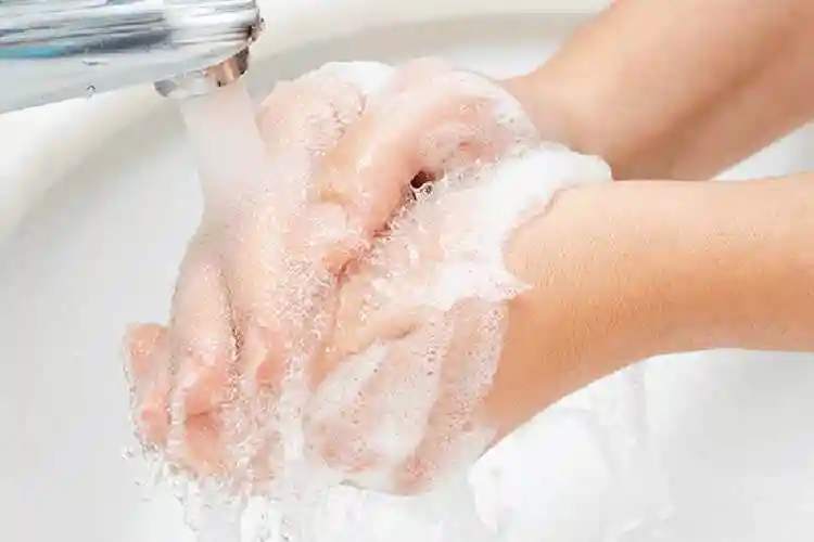水道の蛇口から流れ出る流水で石鹸の泡をつけた手を洗っている写真です。