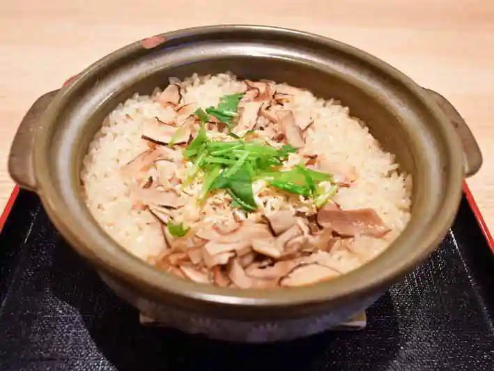 松茸の炊き込みご飯の写真です。土鍋で炊かれた松茸ご飯の上に三つ葉が散らされています。