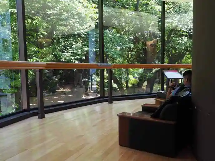 東京国立博物館本館と平成館の途中にあるソファが置かれたラウンジの写真です。庭園に面したガラス壁にそって茶色いソファが並んでいます。庭を眺めながら休んでいる人や昼寝をしている人がいます。