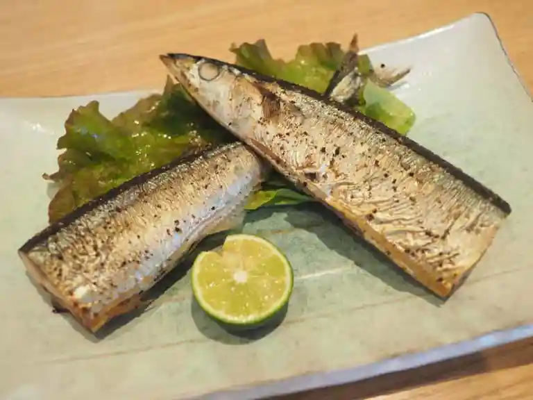 秋刀魚の燻製の写真です。秋刀魚は半分に切られて、四角い皿に盛られています。青いかぼすが添えられています。