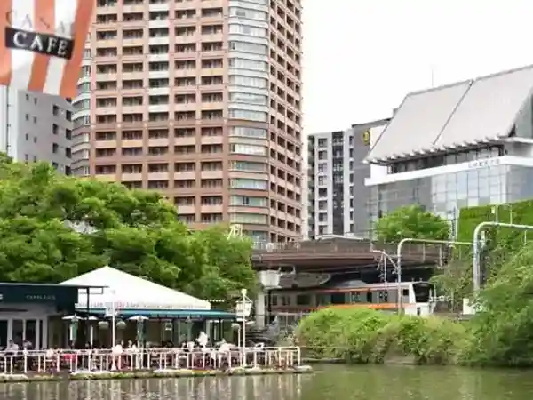 This photo shows the Canal Cafe and the moat bank from the front of the ditch. A Chuo Line train can be seen running along the bank of the trench.