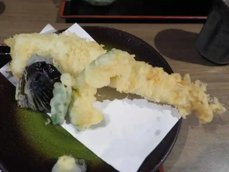 穴子の天ぷらの写真です。一本穴子が揚げられています。ナスとシシトウの天ぷらが添えられています。