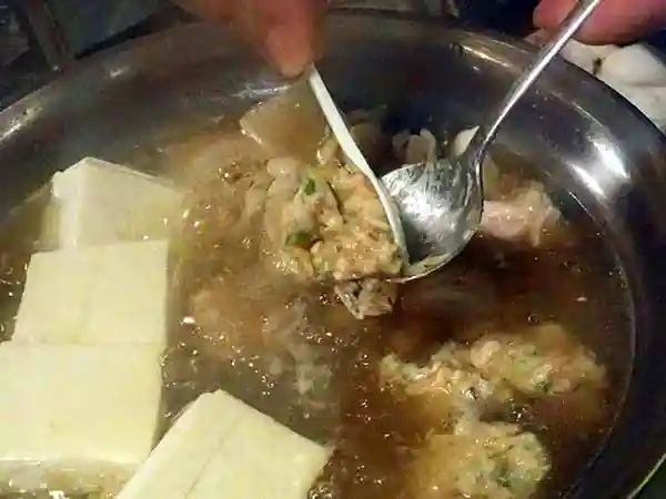 スプーンの上で鶏だんごを丸めて、鍋に落としている写真です。鶏団子には緑色のニラが混ざっています。