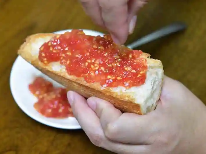 パンにのせたトマトに塩をふりかけている写真です。