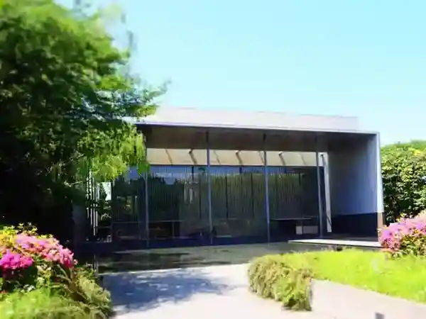 This picture shows the Gallery of Horyuji Treasures at the Tokyo National Museum. The building is modern and has a harmonious design with horizontal and vertical lines and large glass walls. There is an artificial pond in front of the museum, and a granite path leads to the entrance.