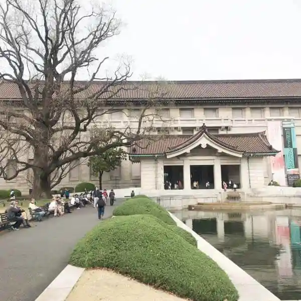 This photo shows the Honkan building at the Tokyo National Museum. It is a reinforced concrete structure with a traditional Japanese-style tiled roof. In front of the Honkan, there is a large lily tree.