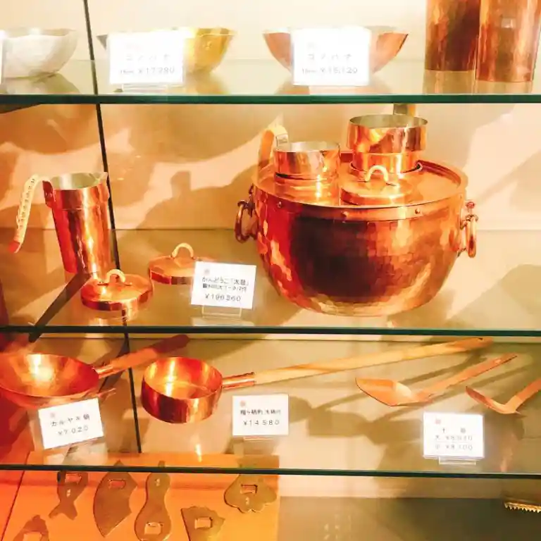 This picture shows shelves lined with various copper products.
On the top shelf is a salad bowl, and below it is a "Kan-Douko," a device used to boil Japanese sake in hot water.
