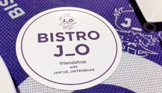 「BISTRO J_O」のコースターの写真です。円形で白色のコースターの上方にはジョーくんという鳥のキャラクターが紫色で描かれています。その下に「「BISTRO J_O」と紫色の文字で印刷されています。