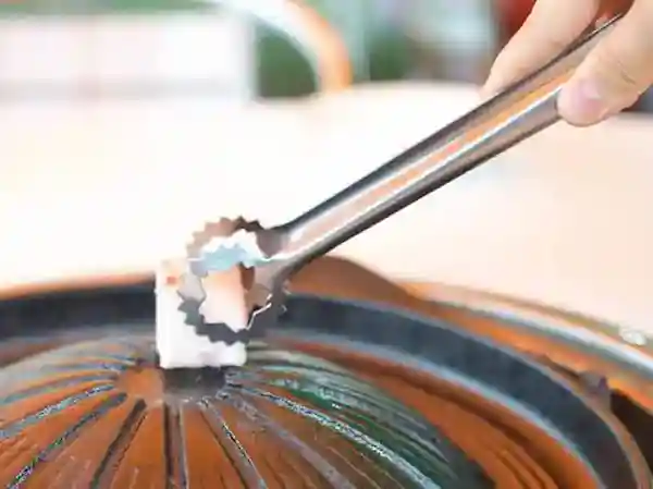 This photo shows beef fat being spread on a Genghis Khan pot. The pot has a raised center resembling a helmet, and the beef fat is pressed onto it using tongs.