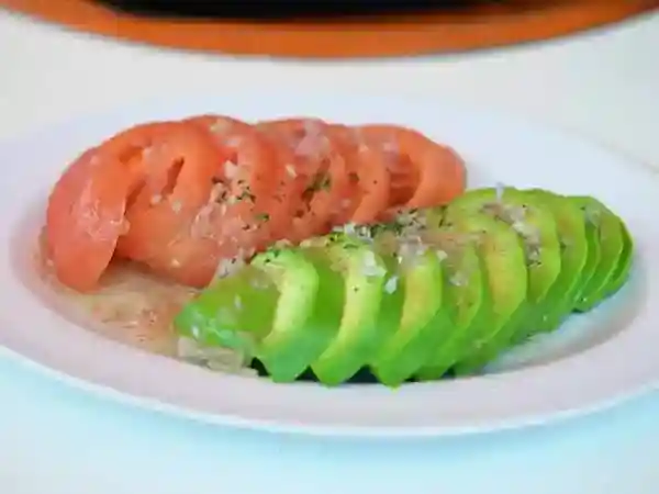 This photo shows an avocado and tomato salad. The red tomatoes and green avocados are served on a white plate, creating a visually appealing contrast. The colorful vegetables and the plate make for a beautiful salad.