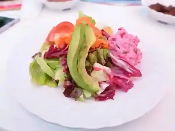 This photo shows a Russian-style garden salad. The ingredients include tomatoes, avocados, and lettuce, and the salad is topped with a sour dressing.