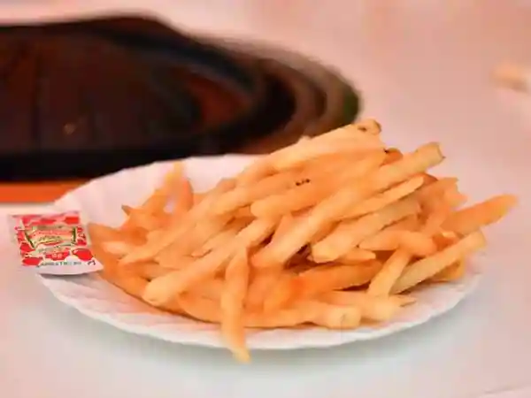This photo shows a plate of french fries with a small bag of tomato ketchup on the side.