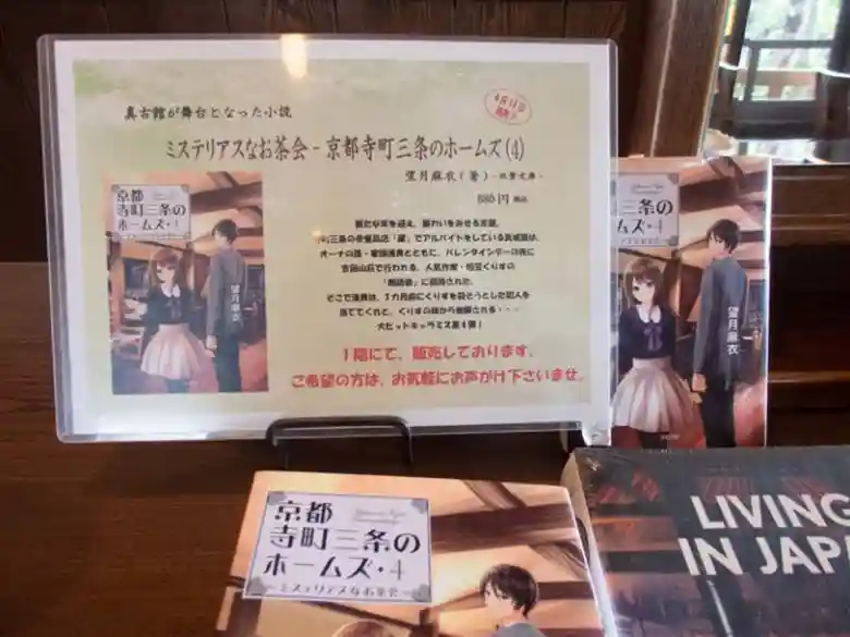 This photo shows a novel titled "Mysterious Tea Party: Holmes of Kyoto: Volume 4," by Mai Mochizuki, displayed in Café Shinkokan. Cafe Shinkokan is the setting.