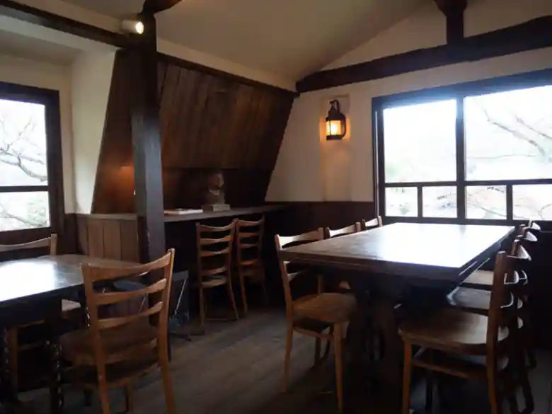 This photo shows a room on the second floor of Café Shinkokan. The wooden floor is shiny black, and antique wooden tables are lined. The interior, lit by lamps, is dimly lit, creating a fantastic atmosphere.