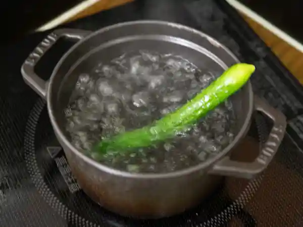 鍋に沸かしたお湯で姫きゅうりを茹でている写真です。熱湯にくぐらすと、きゅうりの色が濃く鮮やかな緑になりました。