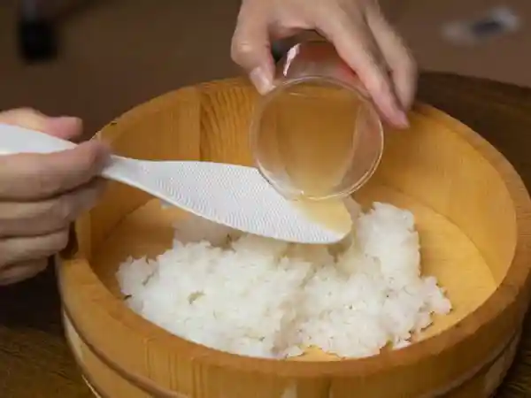 寿司桶に入れた温かいご飯にすし酢をかけている写真です。
