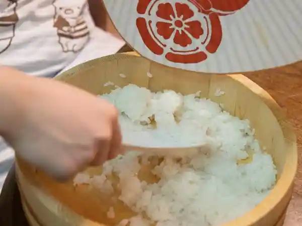ごまと青じそを加えたすし飯をしゃもじで混ぜている写真です。すし飯は木製の寿司桶に入っています。