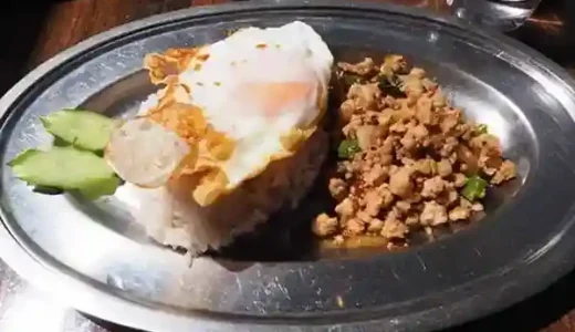 This photograph displays a serving of "Bangkok Gapao Rice" with Jyoshu Mochi Pork on a silver plate, topped with a fried egg.
