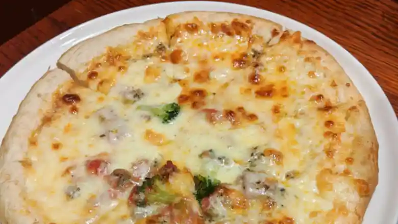 ミックスピザの写真です。直径が25cm位で白い丸皿に盛られています。チーズはところどころ焦げています。