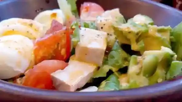 This picture shows a COBB Bowl salad with French dressing. The ingredients include boiled egg, tomato, ham, and lettuce.