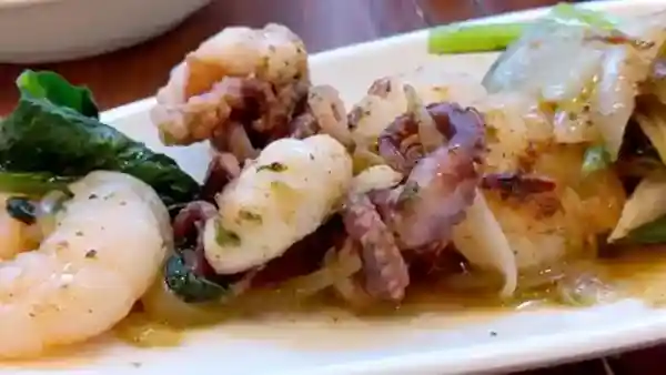 This picture shows a sautéed ocellated octopus and shrimp served with lettuce.