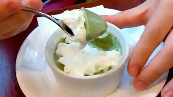 This photo shows a cup of rich green tea pudding served in a white cup about 8 cm in diameter and 6 cm high. The surface is generously topped with cream.