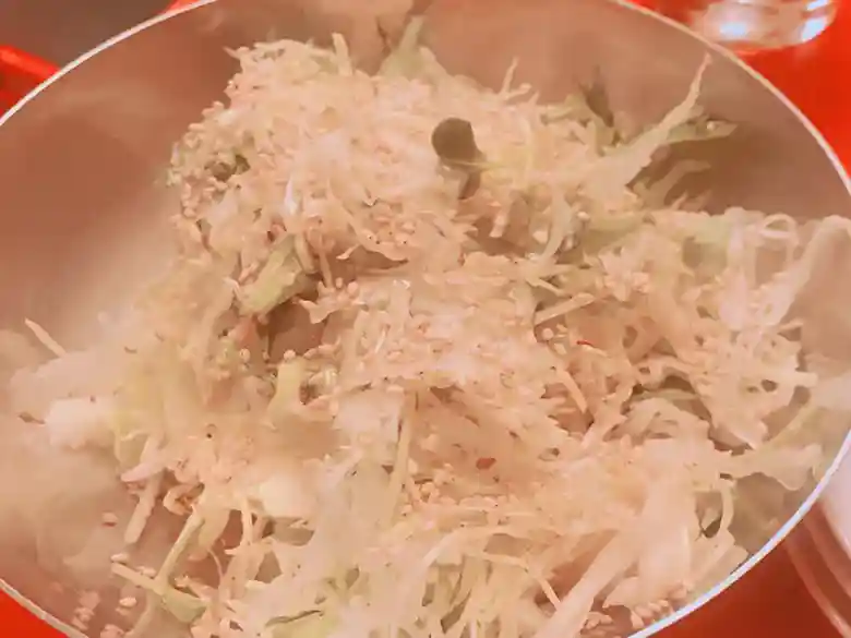 This photo shows a large bowl of cabbage salad in a silver bowl. The salad consists of chopped cabbage.
