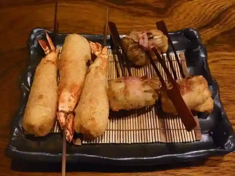 This photo shows three shrimp Kushiage, and three maitake mushroom Kushiage served on a brown square plate.