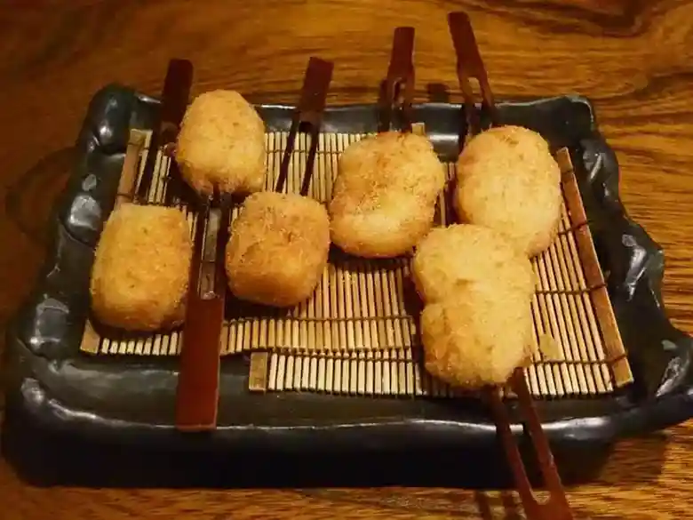 This photo shows the fifth plate of Kushiage: three scallop Kushiage and three apple Kushiage served on a brown square plate.