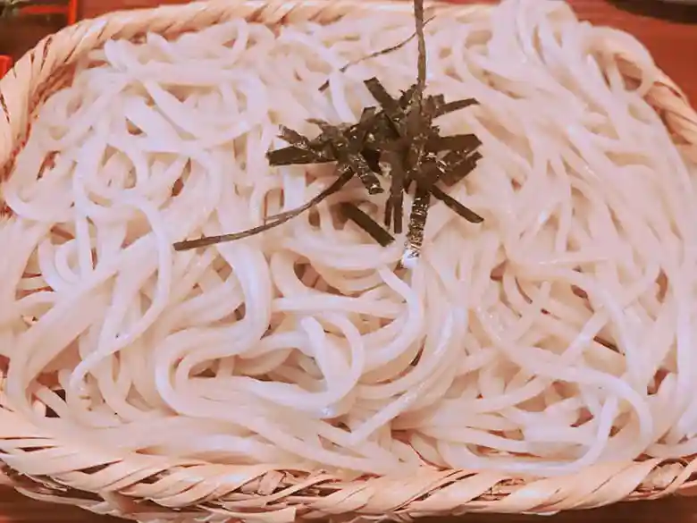 This photo shows Tempura and colander buckwheat noodles. The buckwheat noodles are served on a colander and garnished with chopped seaweed.